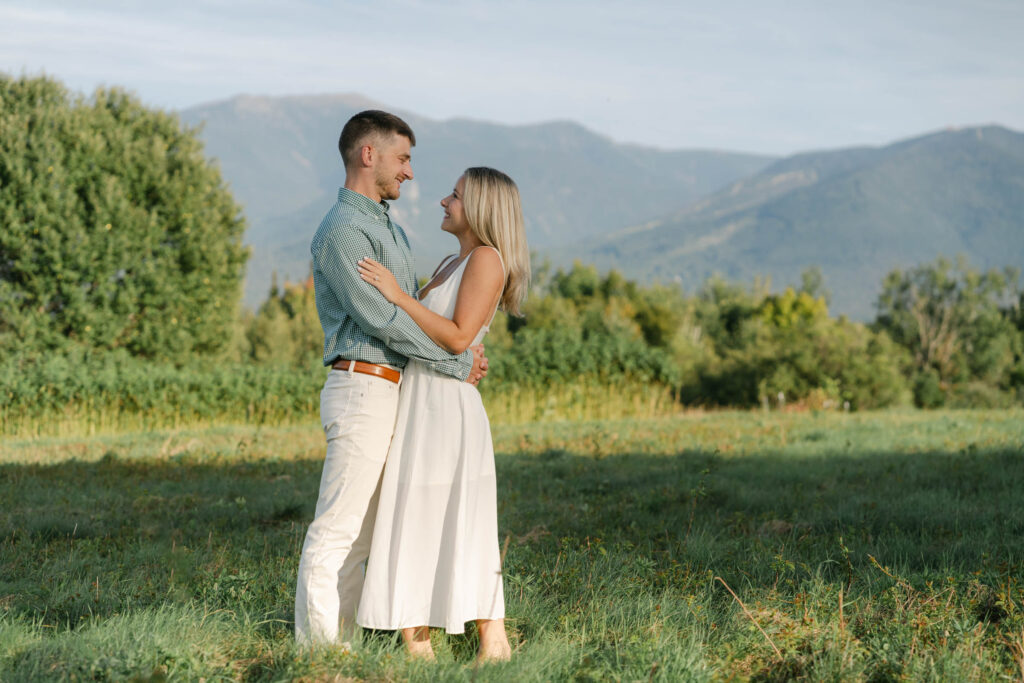 couple standing and looking at each other facing each other with white mountains in view during engagement session