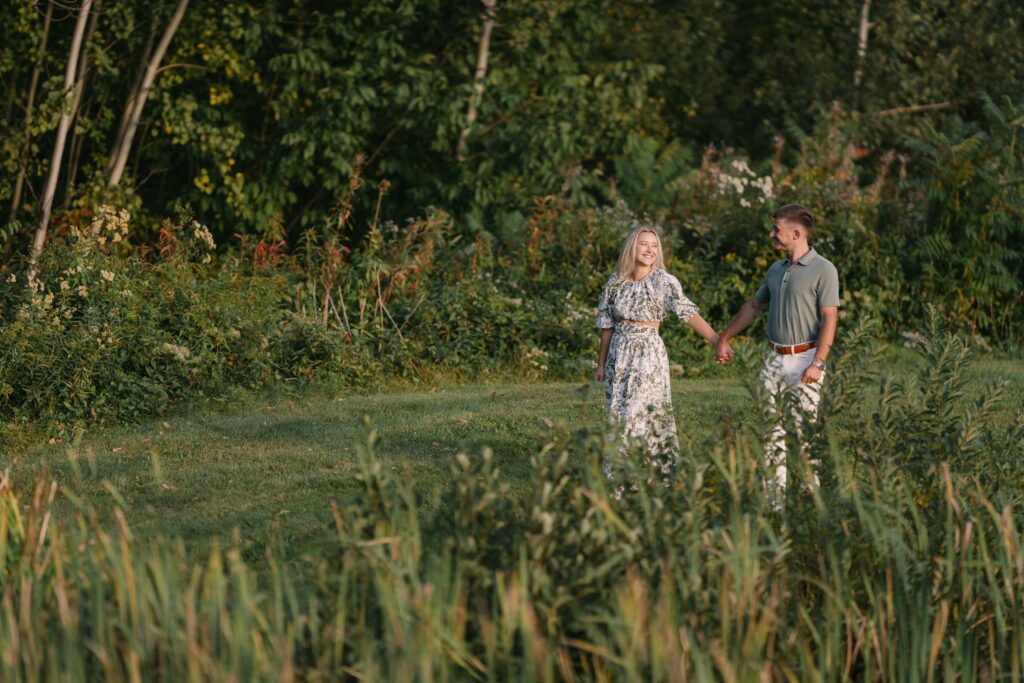 couple walk holding hands through grassy area sugar hill white mountain engagement session