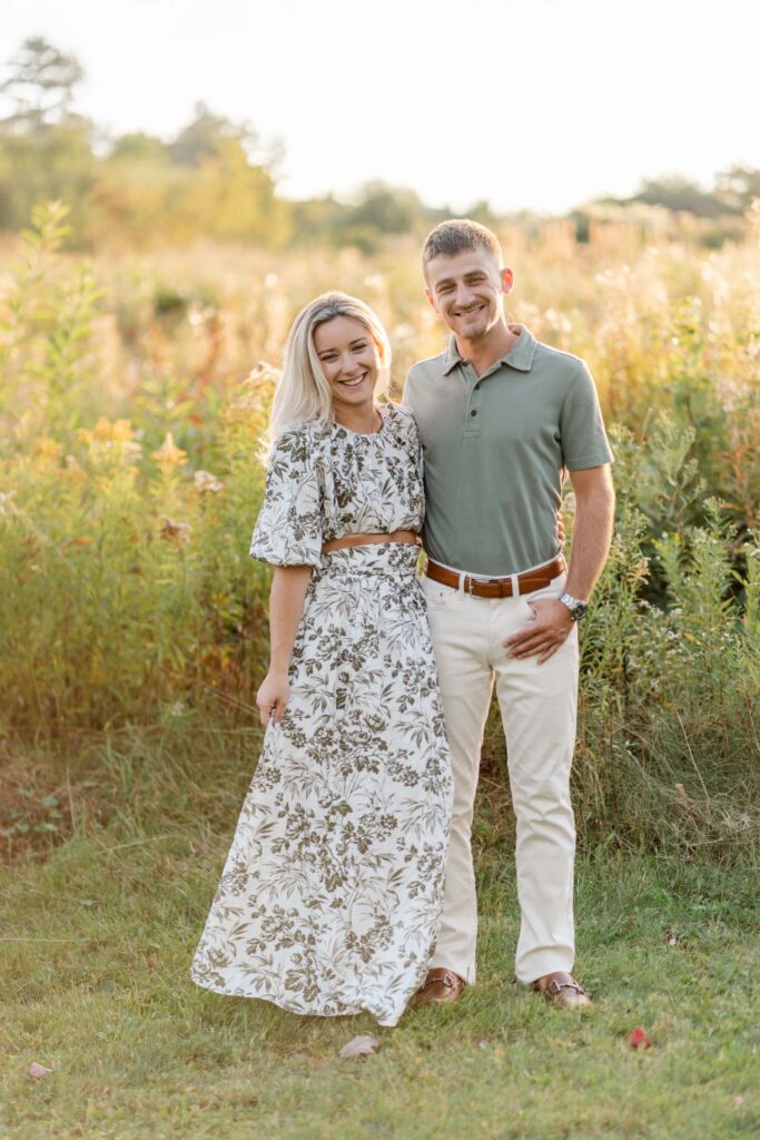 couple look at camera in sunlit field during golden hour sugar hill white mountain engagement session