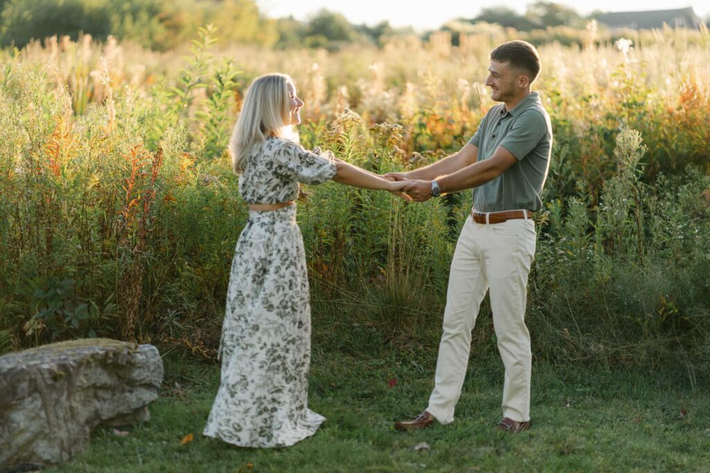 couple hold arms and extend from each other with sunlit golden hour field behind them sugar hill white mountain engagement session