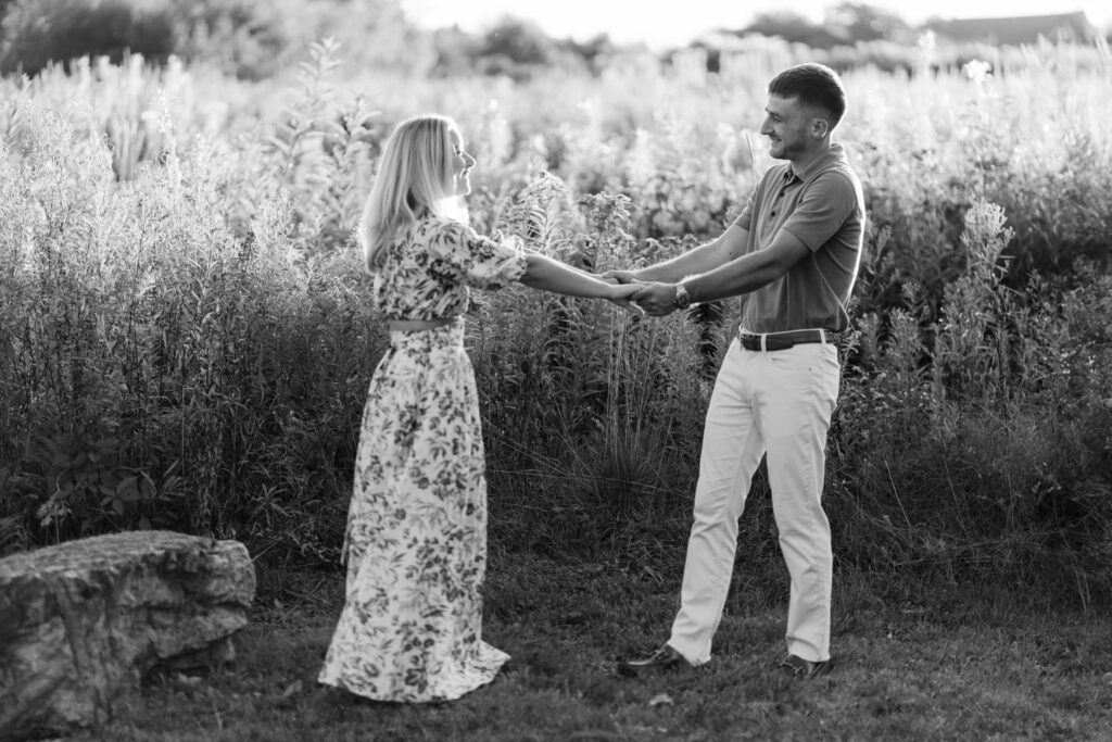 couple hold arms and extend from each other with sunlit golden hour field behind them sugar hill white mountain engagement session