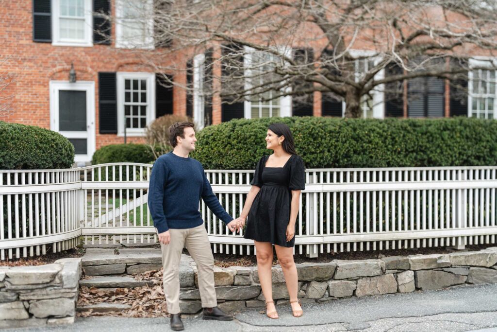 couple standing in front of house and fence during woodstock vermont engagement session