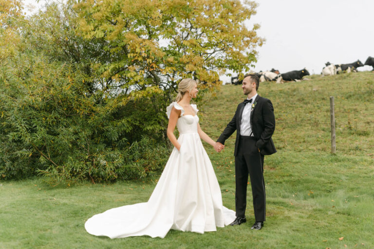 Fall Vermont Wedding at The Inn at Round Barn Farm, the bride and groom stand near the field with cows in the distance