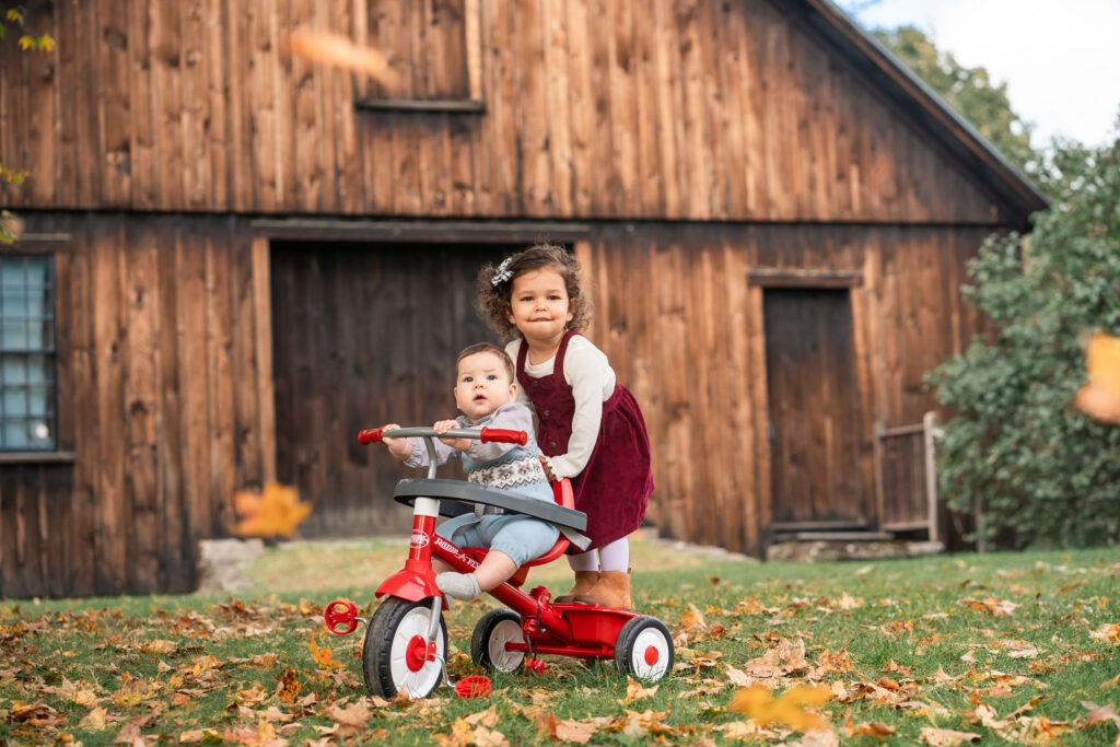October Family Photos in Woodstock Vermont, kids on tricycle with leaves falling down