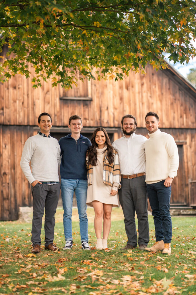 adult children and siblings standing together during portrait in front of antique barn
