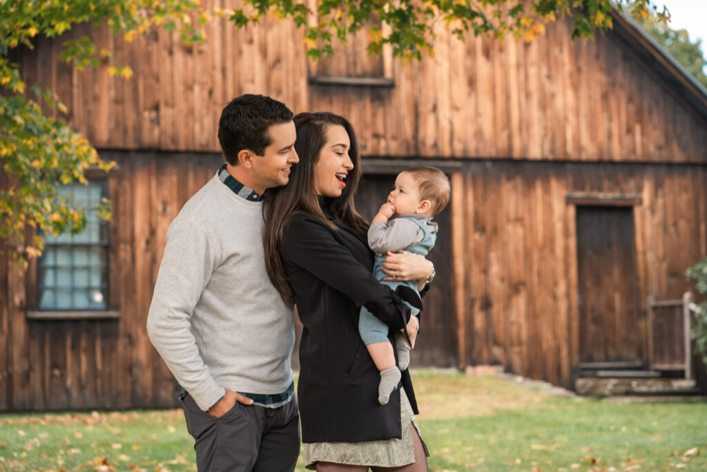 Parents holding baby in front of wooden barn during woodstock vermont fall family photo session