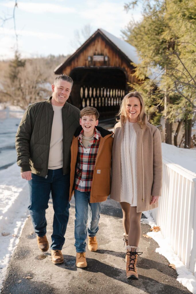 Winter photo session in Woodstock Vermont during wassail weekend - the family walk down the street with a covered bridge behind them