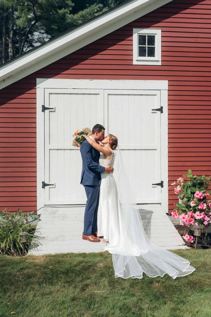 Couple kissing in front of white doors of red barn