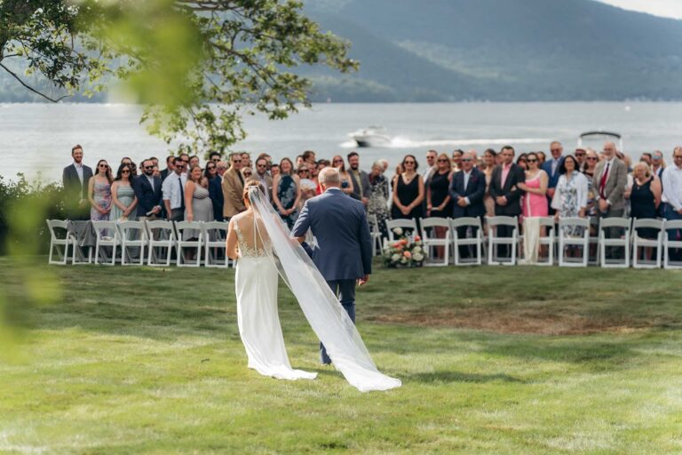 Bride and father walk toward ceremony with lake in distance at Newfound Lake Wedding